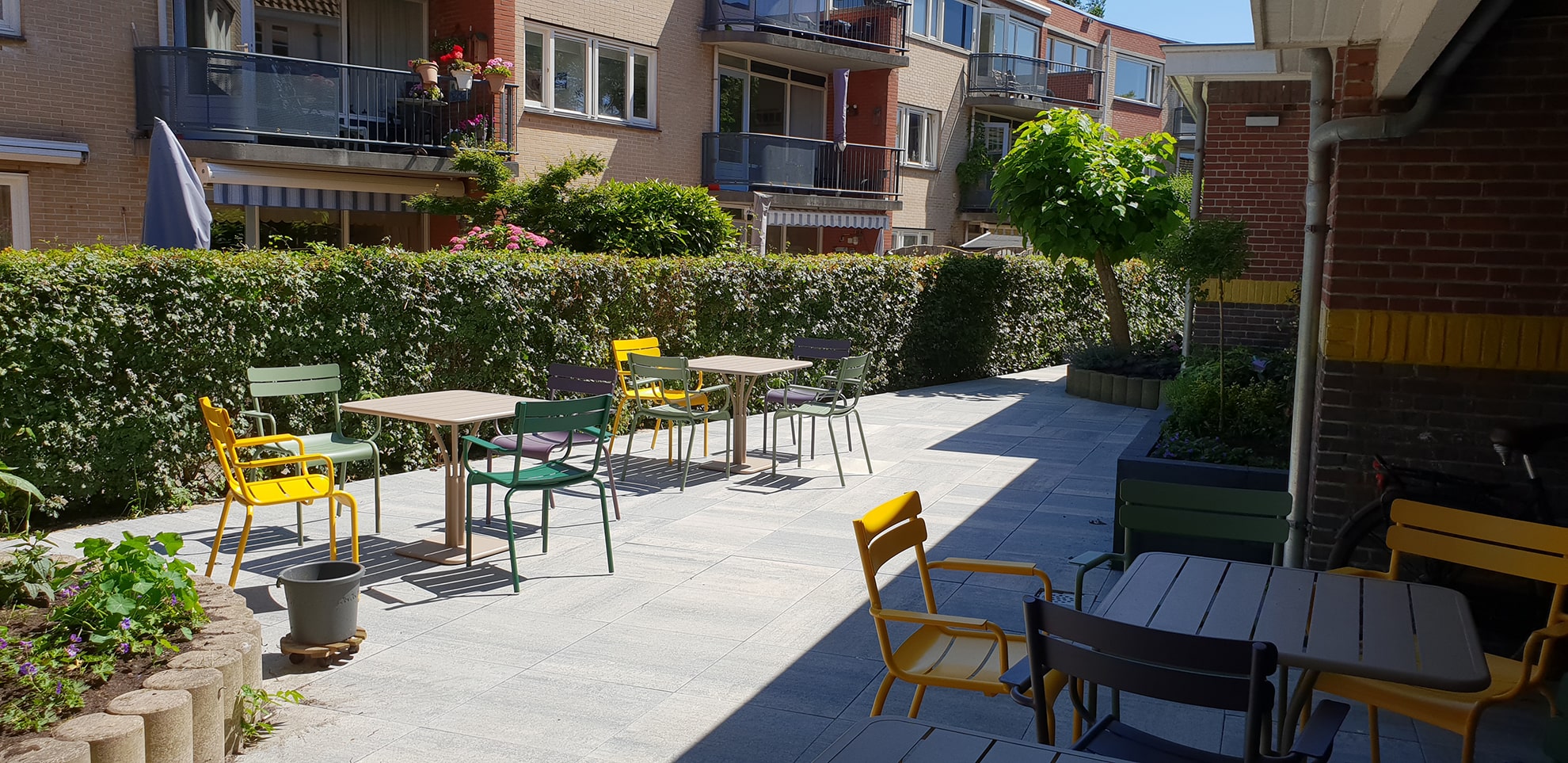de tuin van de Molenwerf met zitjes van tafels en stoelen in groen en geel, groene heggen en bomen