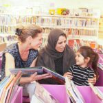 een vrijwilliger van de VoorleesExpress met een moeder en dochter in de bibliotheek