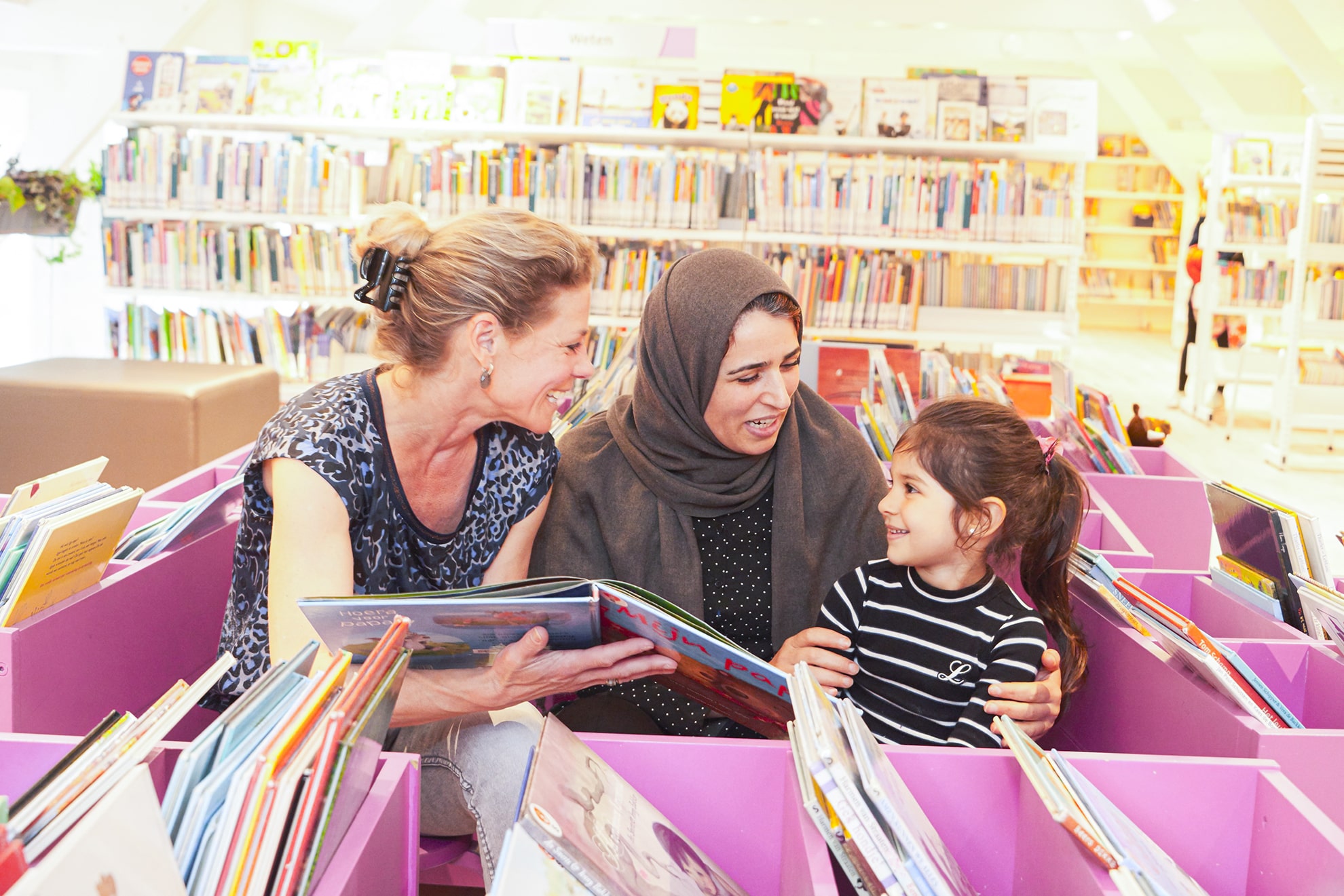 een vrijwilliger van de VoorleesExpress met een moeder en dochter in de bibliotheek